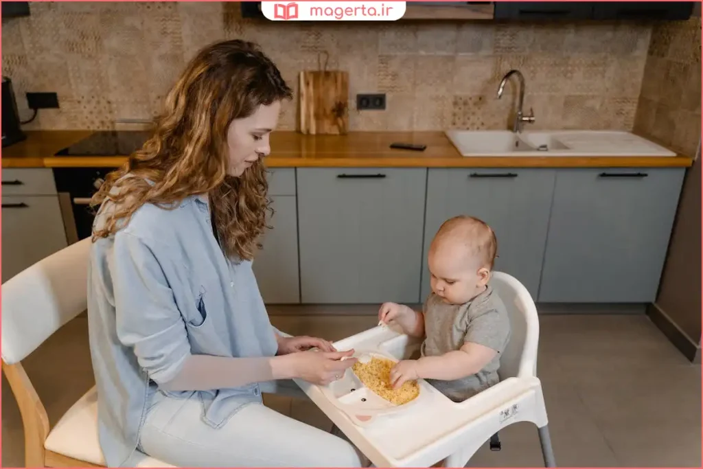نوزاد در صندلی غذاخوری در حال امتحان اولین غذای کمکی