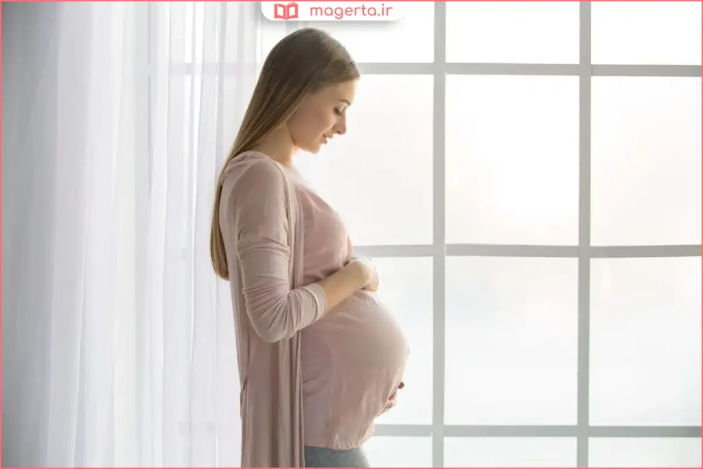 مادر باردار در حال نوازش شکم خود با لبخند آرام برای ارتباط با جنین