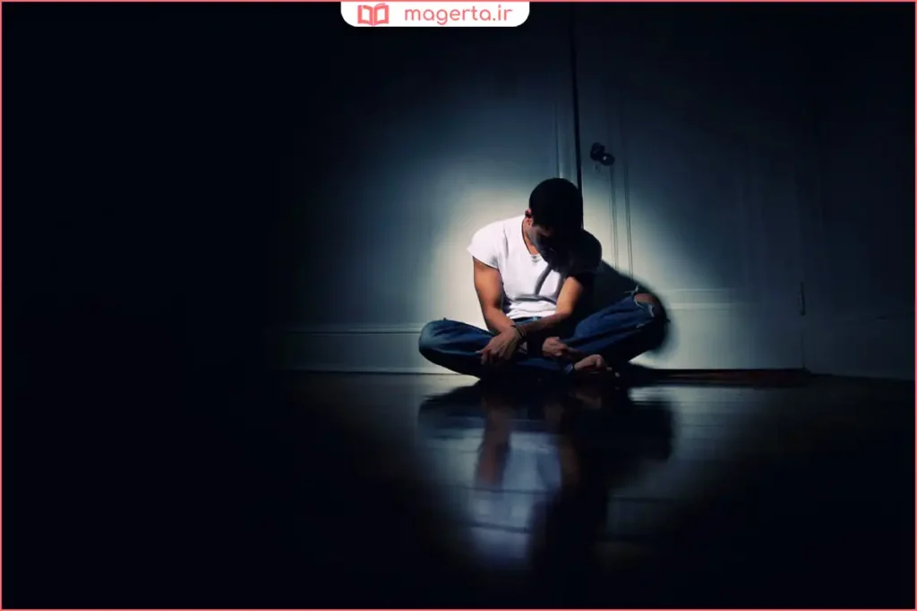 فردی نشسته تنها در اتاق با نور کم و حالت اضطراب