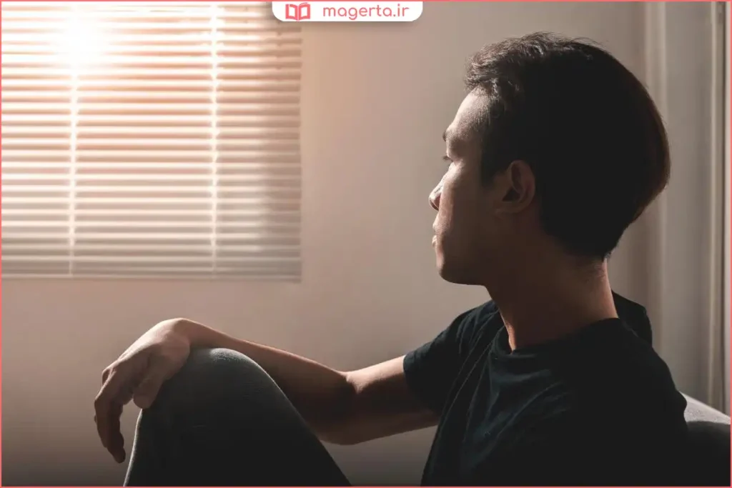 فردی نشسته در اتاق با حالت غمگین و نگاه پایین نشانه احساس تنفر از خود